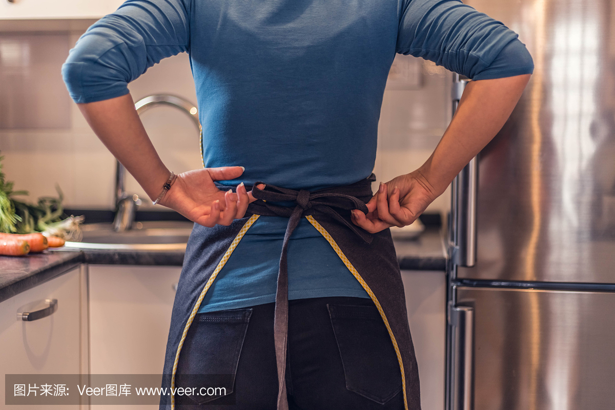 紧缩的围裙。厨房里穿着围裙的漂亮女人。